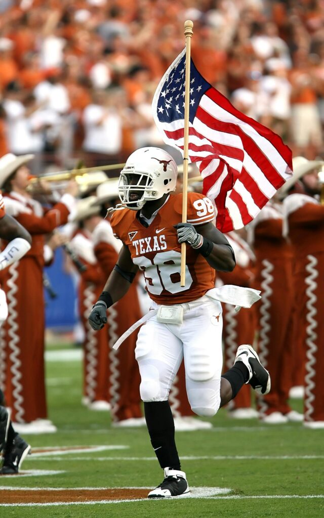 Football player runs with American flag at a Texas game, showcasing team spirit and national pride.